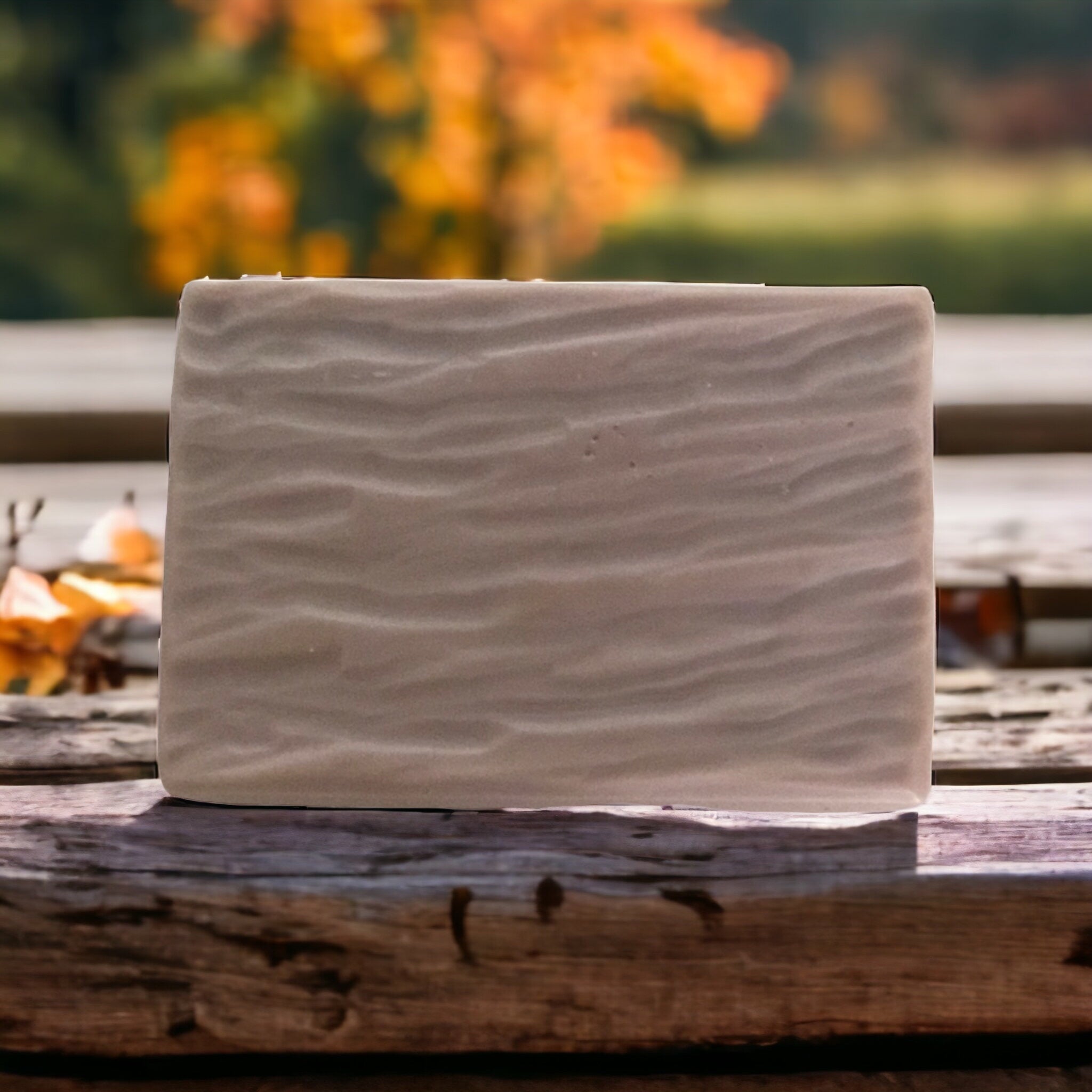 Photo of brown rectangular soap on a wooden tabel with fall leaves in the background for display