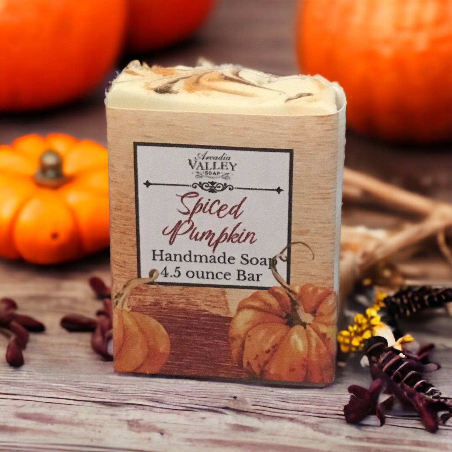 Spiced pumpkin soap with decorative paper wrapper sitting on a wooden table with pumpkins and spices on display