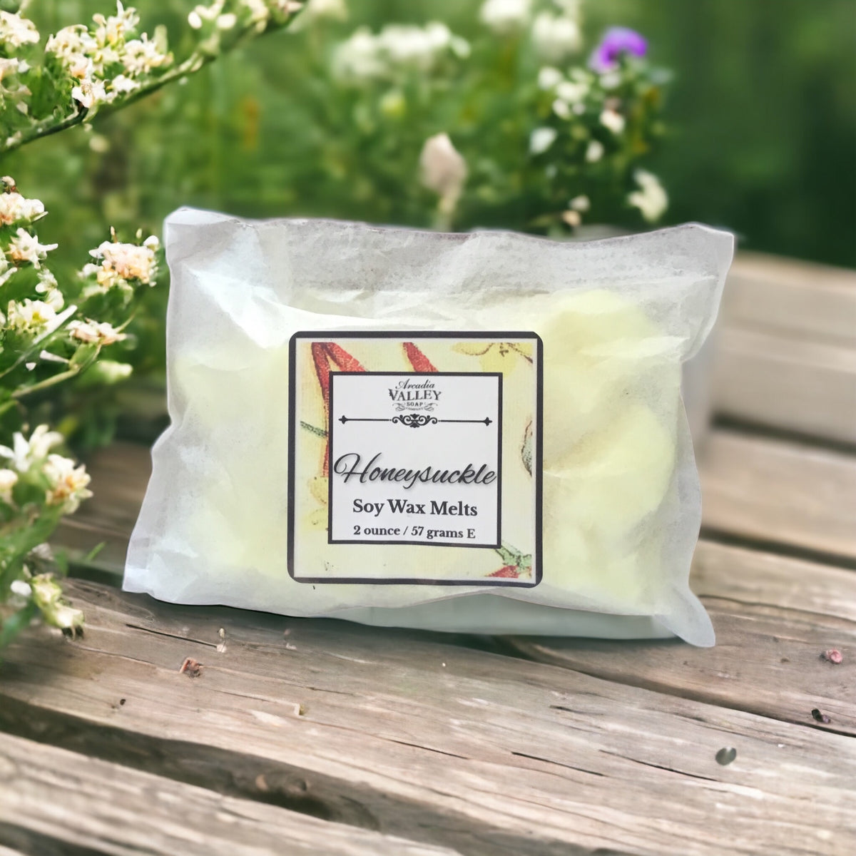 Paper pouch of honeysuckle wax melts on a wooden table with flowers on side.